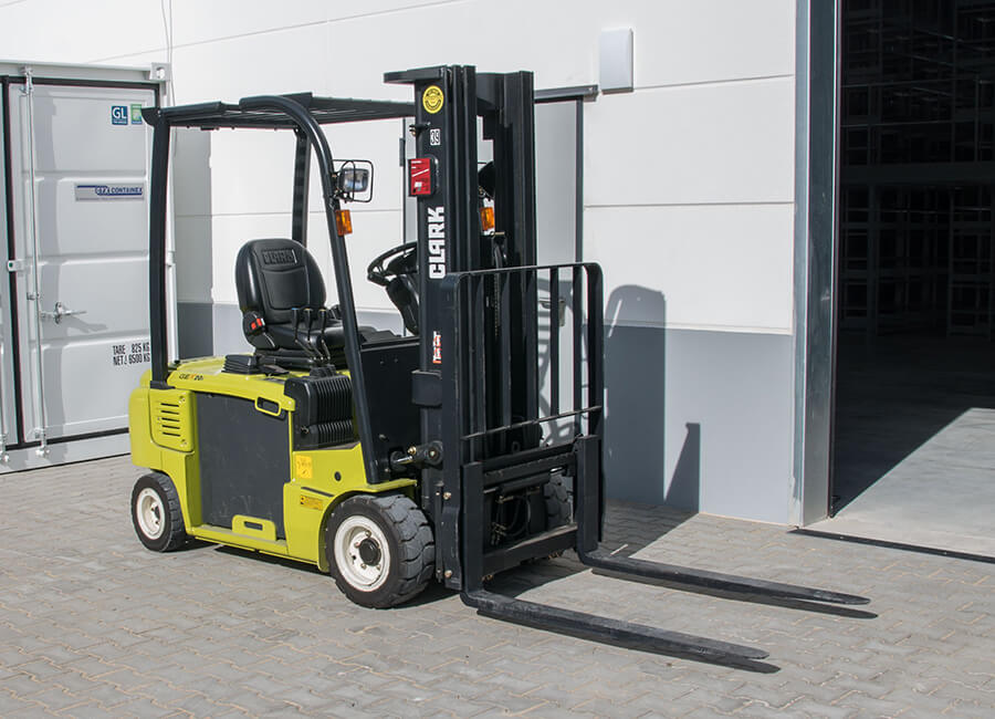 Yellow electric forklift with solid pneumatic tires on paved yard outside a warehouse