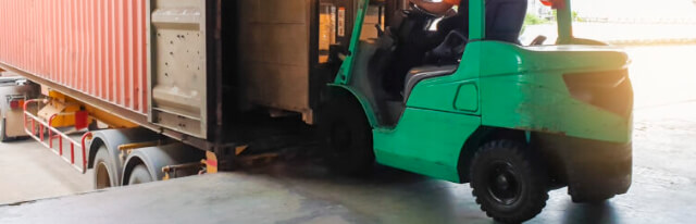 Forklift loading a freight container at a warehouse dock